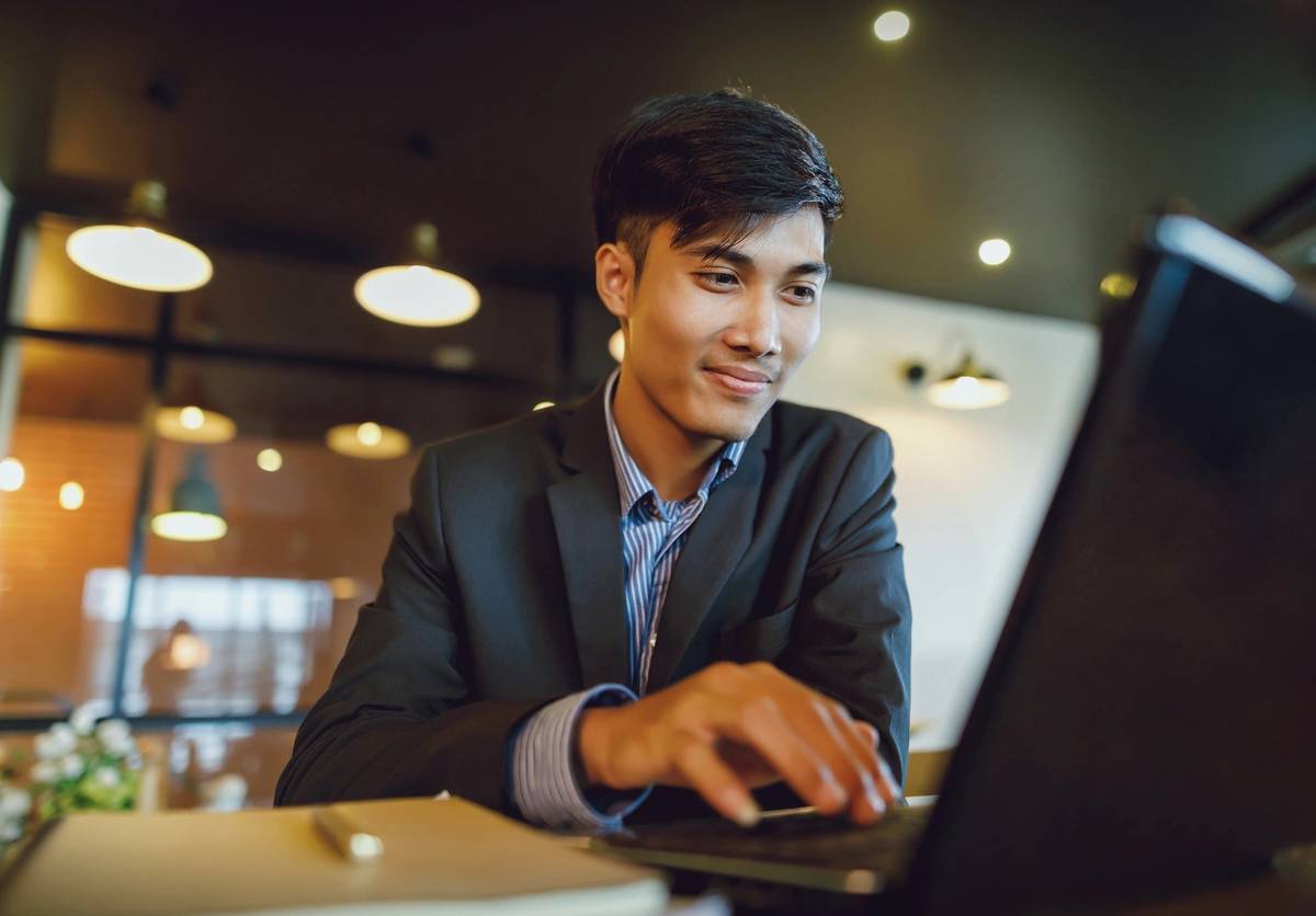 Smiling asian businessman in suit working with laptop